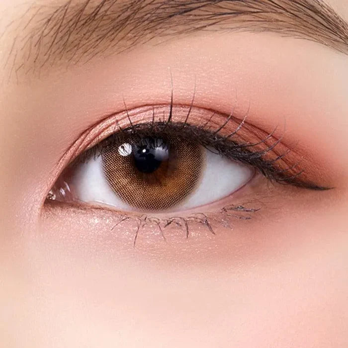 A close-up of a person’s brown eye with natural makeup and long lashes, featuring Olola Able Brown lenses by Olola for dark eyes—designed to enhance your look with or without a myopia prescription.