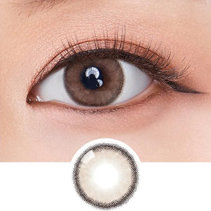 Close-up of an eye wearing Olola Dearsome Milk Brown contact lens by Olola, showing its detailed brown and black gradient iris pattern. An enlarged image highlights the design. Available in non-prescription and myopia prescription options.