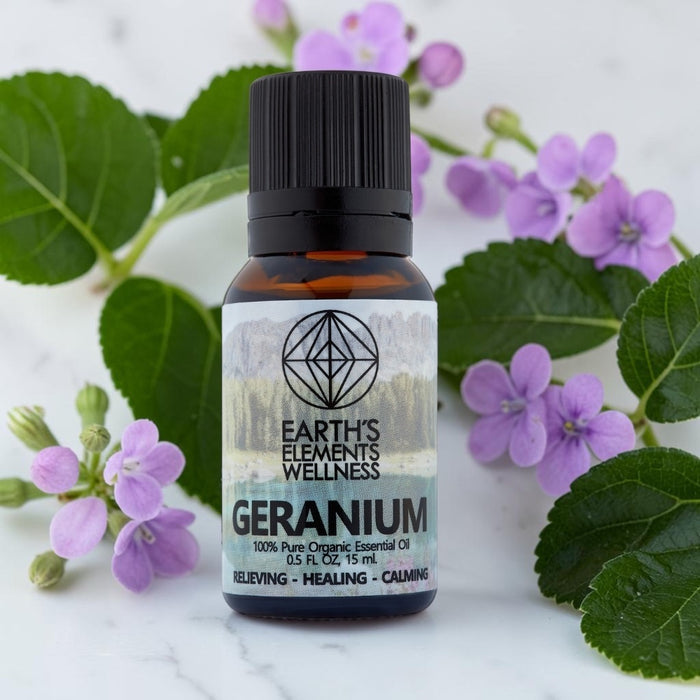 Bottle of Earth's Elements Wellness Geranium essential oil with flowers and leaves on a light background