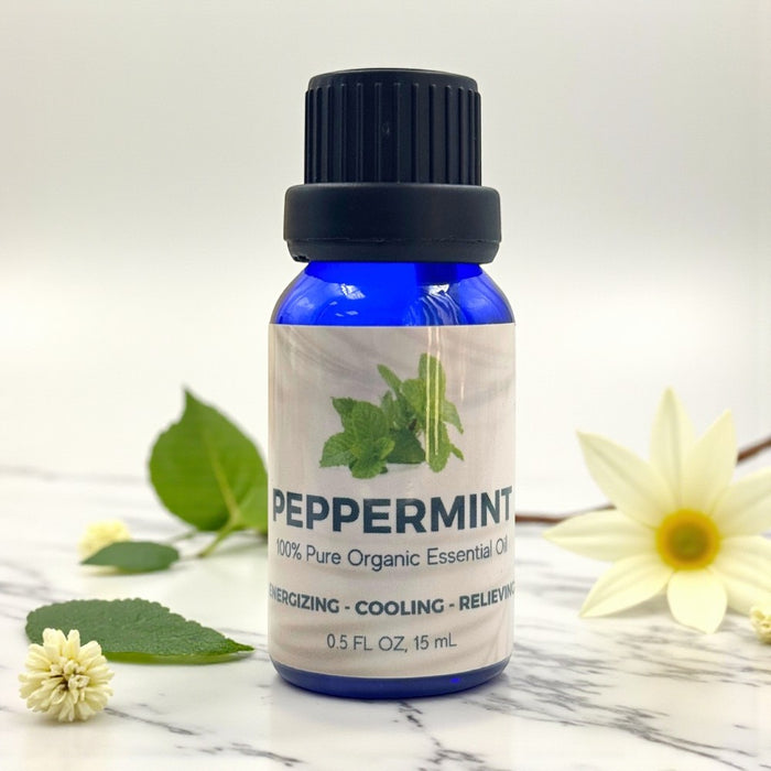 Bottle of peppermint essential oil with flowers and leaves on a marble surface