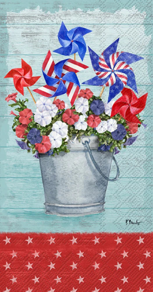 A guest towel featuring an illustration of a galvanized bucket filled with colorful flowers, topped with star-spangled pinwheels, set against a rustic woodgrain backdrop with a starry red trim.