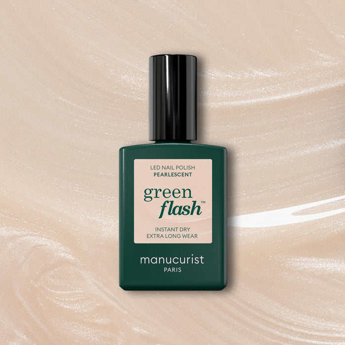 A bottle of Manucurist Pearlescent nail polish with a dark green cap and label rests on a shimmering beige gel background. The label reads: “green flash, instant dry, extra long wear, manucurist Paris.”.