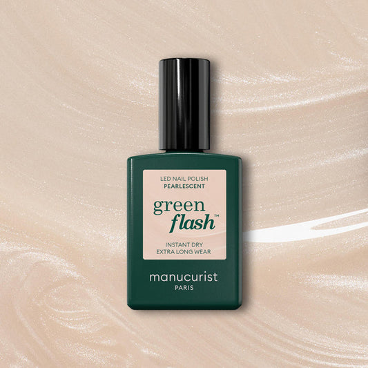 A bottle of Manucurist Pearlescent nail polish with a dark green cap and label rests on a shimmering beige gel background. The label reads: “green flash, instant dry, extra long wear, manucurist Paris.”.