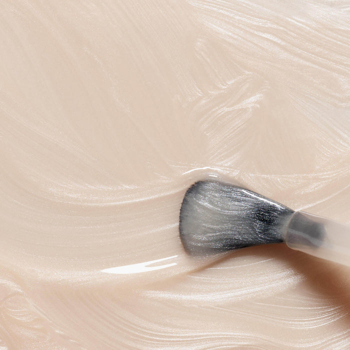 A close-up of a makeup brush blending Manucurist’s Pearlescent, a creamy light beige cosmetic with pink undertones and a smooth, glossy texture.