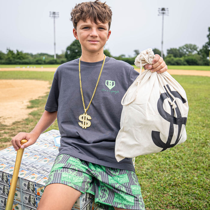 Young boy in a sports field holding a bag of money, wearing a gold necklace and gray shirt.