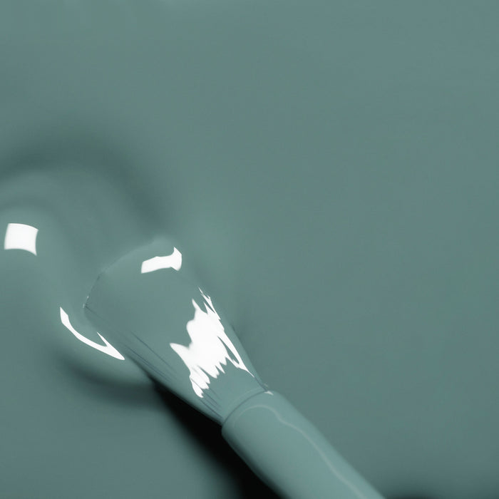 A close-up of a Manucurist Sage nail polish brush coated in glossy, sage green polish, showing reflective highlights and smooth, even coverage on the surface below.