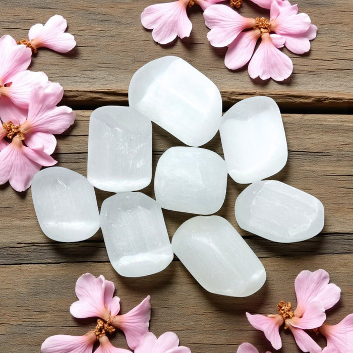 White tumbled selenite on a wooden surface with pink flowers