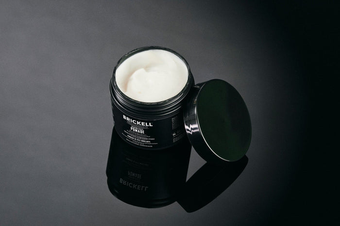 Open jar of Brickell men's pomade on a reflective dark surface.
