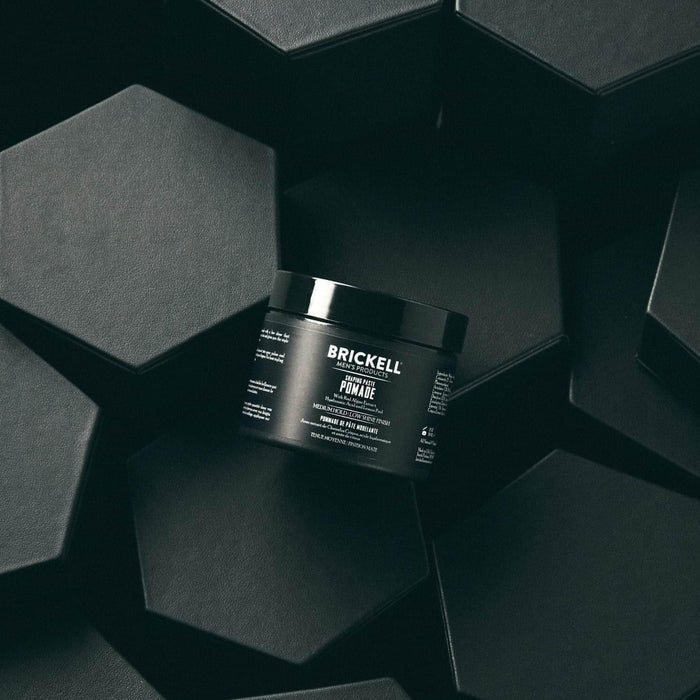 Brickell Men's Products hair pomade in black container on dark geometric background