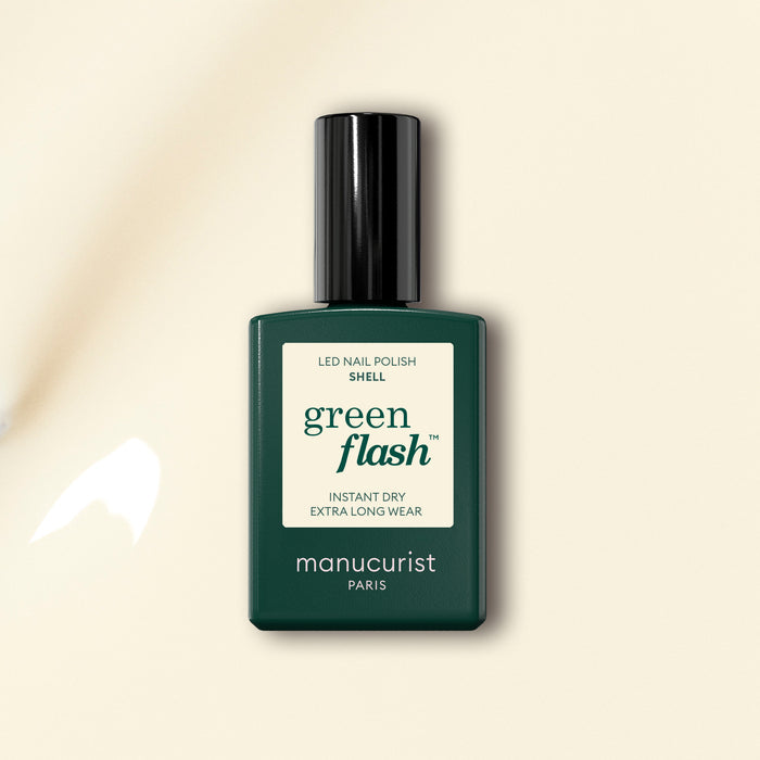 A bottle of Manucurist nail polish in the shade Shell, featuring a dark green label and black cap, is displayed on a light beige background.