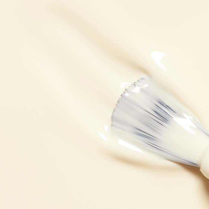 A close-up of Manucurist's Shell makeup brush blending creamy, light beige foundation on a smooth surface, paired with touches of minimalist nail polish for an effortlessly chic finish.
