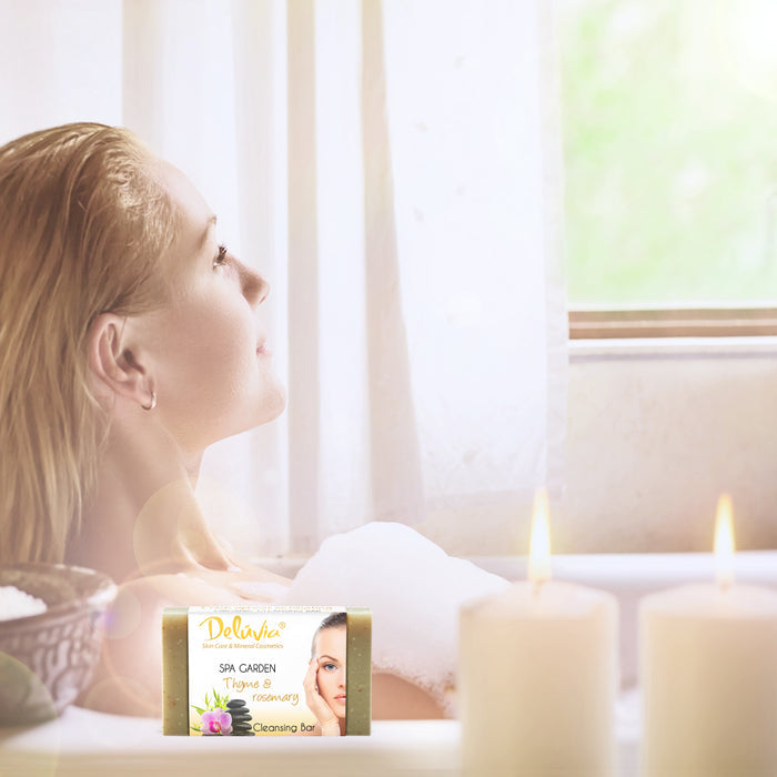 A woman in a bubble bath with candles and a bar of Deluvia soap