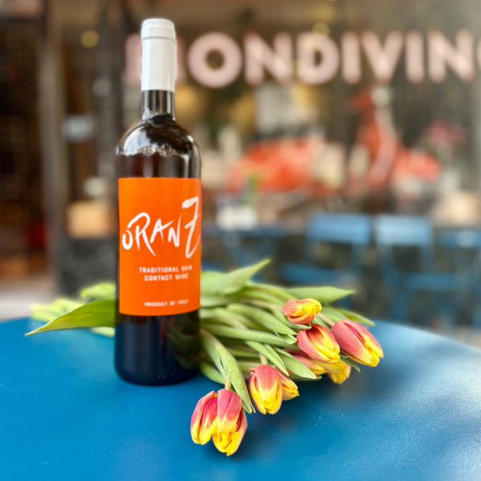 Wine bottle with orange label and white cap beside yellow and pink tulips