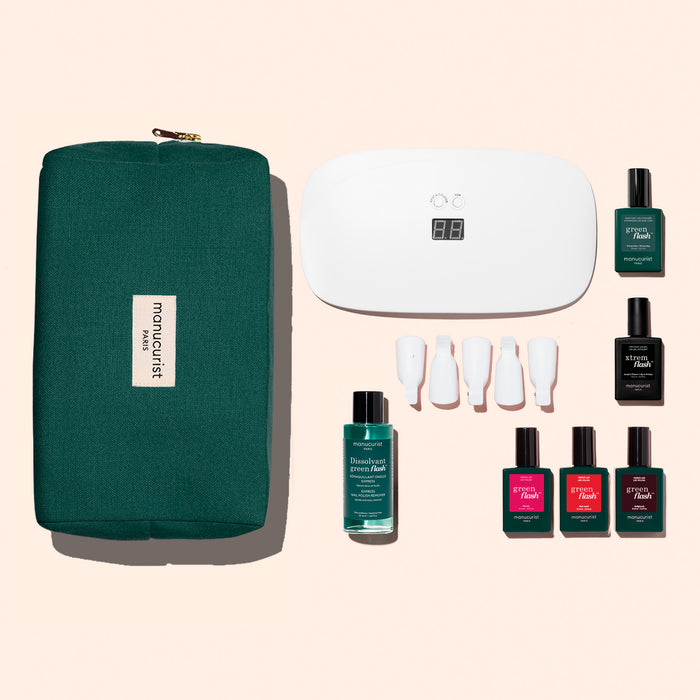 The Manucurist Starter Kit includes a green zippered pouch, white LED nail lamp, four white nail tools, remover bottle, and six gel polishes for an ultra-glossy manicure—all neatly arranged on a light background.