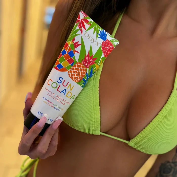 Zbliżenie na kobietę w zielonym stroju kąpielowym trzymającą tubę Onyx Suncolada Bronzer.