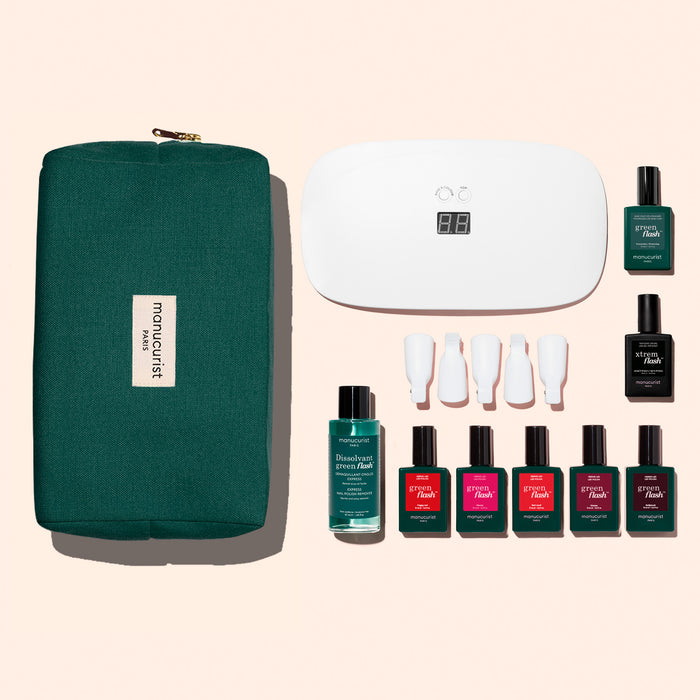 The Manucurist Super Starter Kit features a green zippered pouch, white LED nail lamp, four nail polishes (including a vitaminized base), nail polish remover, and four white tools arranged on a light background.