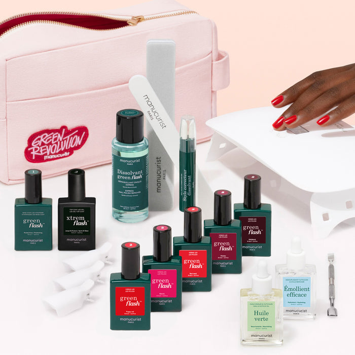 The Manucurist Super Ultimate Kit, featuring Green Flash gel polish, remover, nail oils, files, and a vitamin-enriched base coat with a pink bag. A hand with red nails showcases an ultra-glossy look under a white LED lamp.