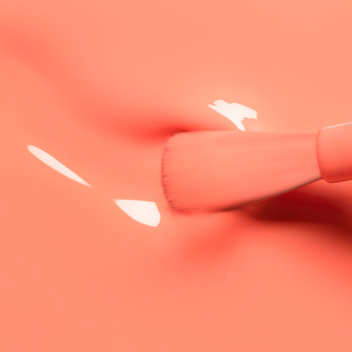 A close-up of a Manucurist Tangerine makeup brush applying glossy coral cream on a smooth, matching background, creating soft reflections and subtle texture reminiscent of neon orange polish.