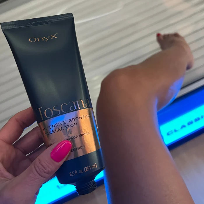 Kobieta trzyma balsam Onyx Toscana podczas sesji w solarium, widoczne niebieskie światło i opalona noga, produkt do intensywnego brązowienia skóry