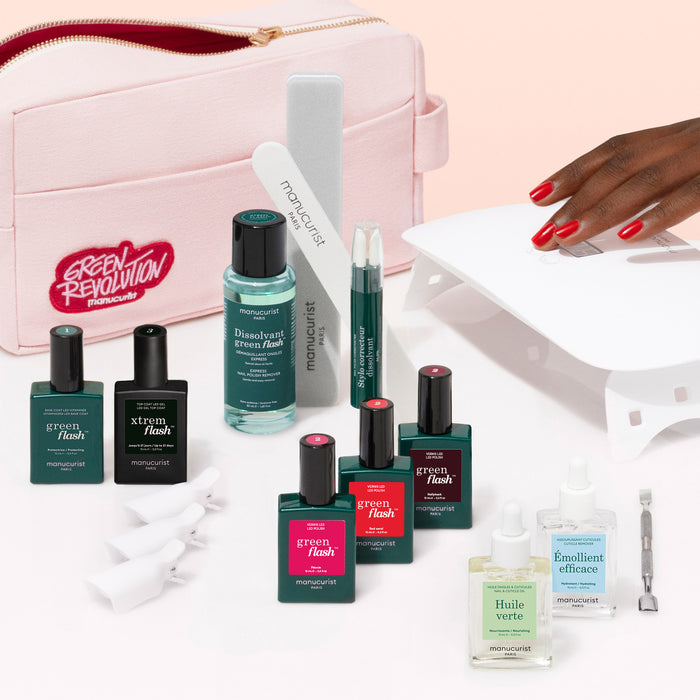 The Manucurist Ultimate Kit features a pink cosmetic bag surrounded by nail care must-haves: vitamin-infused base coat, gel polish, remover, pen applicators, nail file, UV lamp, and a manicured hand with an ultra-glossy finish.