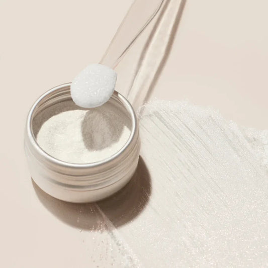 A small jar of Manucurist White Glazed Effect Powder sits open on a light surface, with a clear spoon holding a scoop above it and a streak of powder beside—ideal for creating stunning white glazed nails in your next manicure.