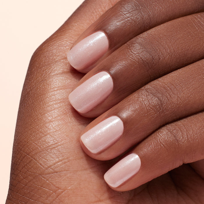 A close-up of a hand with medium-dark skin, featuring short, neat nails painted pale pink and topped with Manucurist's White Glazed Effect Powder for a subtle shimmer and elegant manicure.