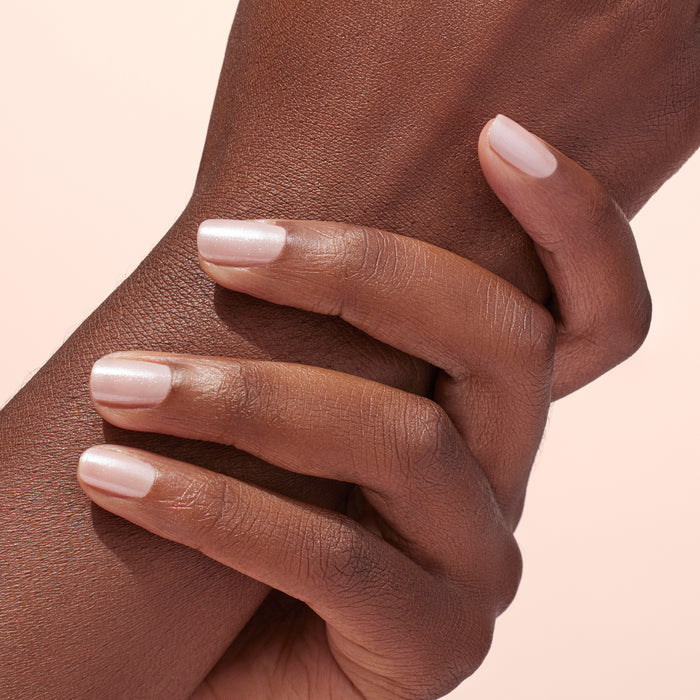 A close-up of a hand with nails manicured using Manucurist White Glazed Effect Powder, gently holding the opposite wrist against a light, neutral background.