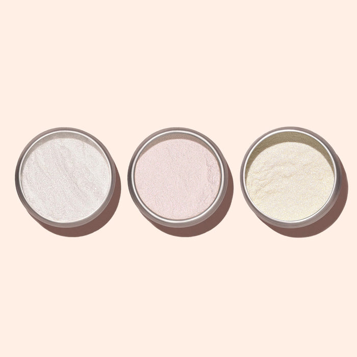 Three small round containers of Manucurist White Glazed Effect Powder, displaying white, pink, and pale yellow shades for a pearlescent manicure, are neatly arranged in a row on a light beige background.